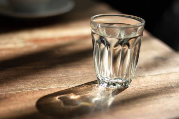 A clear glass of water on a wooden table bathed in soft morning light